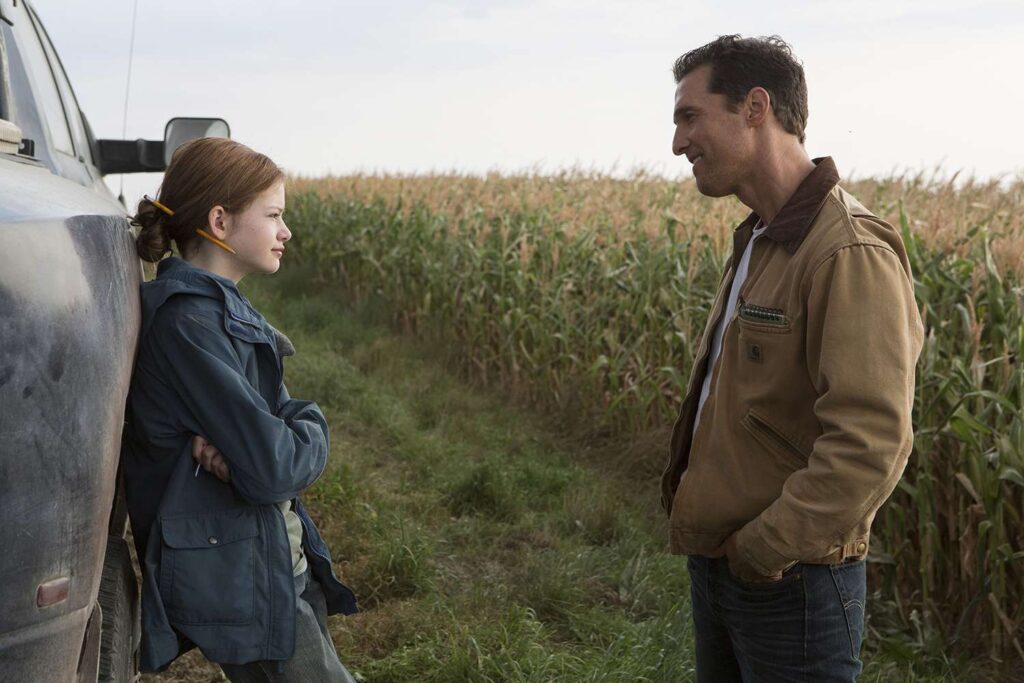 Seorang ayah dan putrinya berdiri di tepi ladang jagung, saling menatap dengan penuh kehangatan dalam adegan film Interstellar karya Christopher Nolan.
