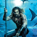 Aquaman berdiri tegak dengan trisula di tangannya, dikelilingi oleh berbagai jenis ikan hiu di bawah laut, menampilkan kekuatannya sebagai Raja Atlantis.