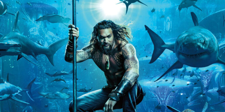 Aquaman berdiri tegak dengan trisula di tangannya, dikelilingi oleh berbagai jenis ikan hiu di bawah laut, menampilkan kekuatannya sebagai Raja Atlantis.