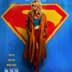 Poster film Supergirl (2026) dengan karakter utama Kara Zor-El mengenakan kostum Supergirl lengkap dengan jaket panjang, berpose di depan latar belakang logo Superman yang ikonik.