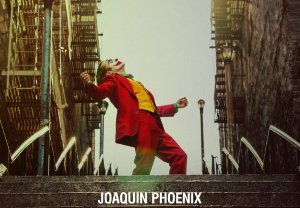 Joaquin Phoenix sebagai Joker berdiri di tangga kota, mengenakan jas merah ikonik dengan ekspresi penuh emosi, dari film Joker (2019).