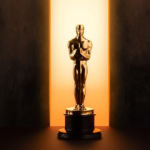 Patung Oscar emas berdiri di atas podium dengan cahaya dramatis dari belakang